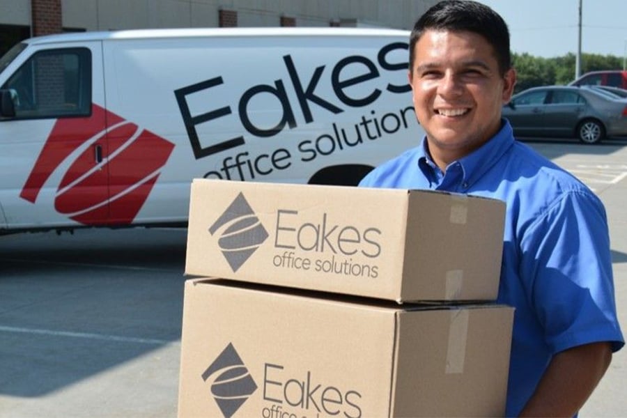 An Eakes employee carrying boxes of office supplies standing near the Eakes official van.