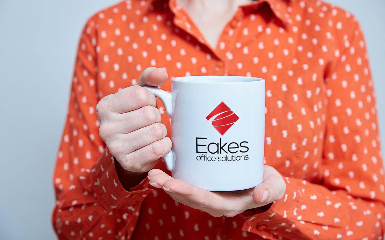 A person holding a white mug with Eakes logo on it.